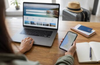 Laptop en smartphone waarop je vakanties en bestemmingen kunt vergelijken, met reisnotities en bagage op de achtergrond