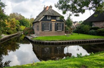 Thatched roof house by a canal with reflection
