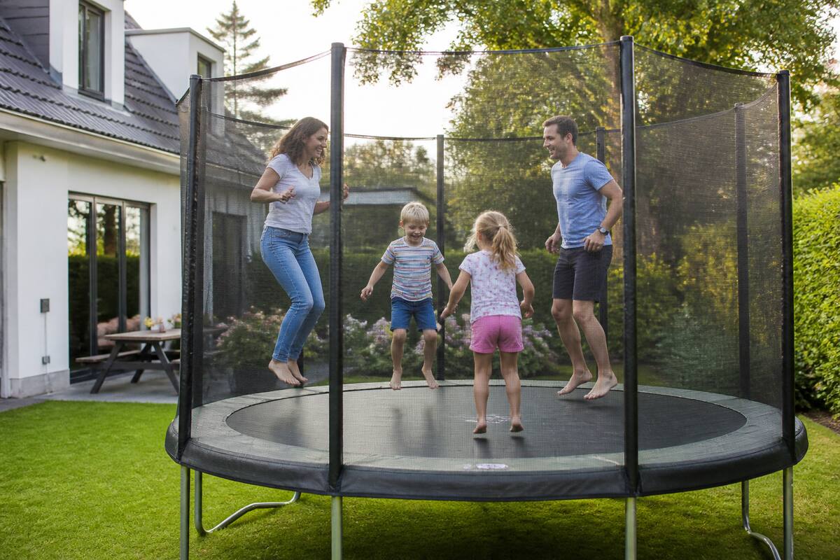 Kinderen springen op een trampoline met veiligheidsnet en randkussen in een tuin